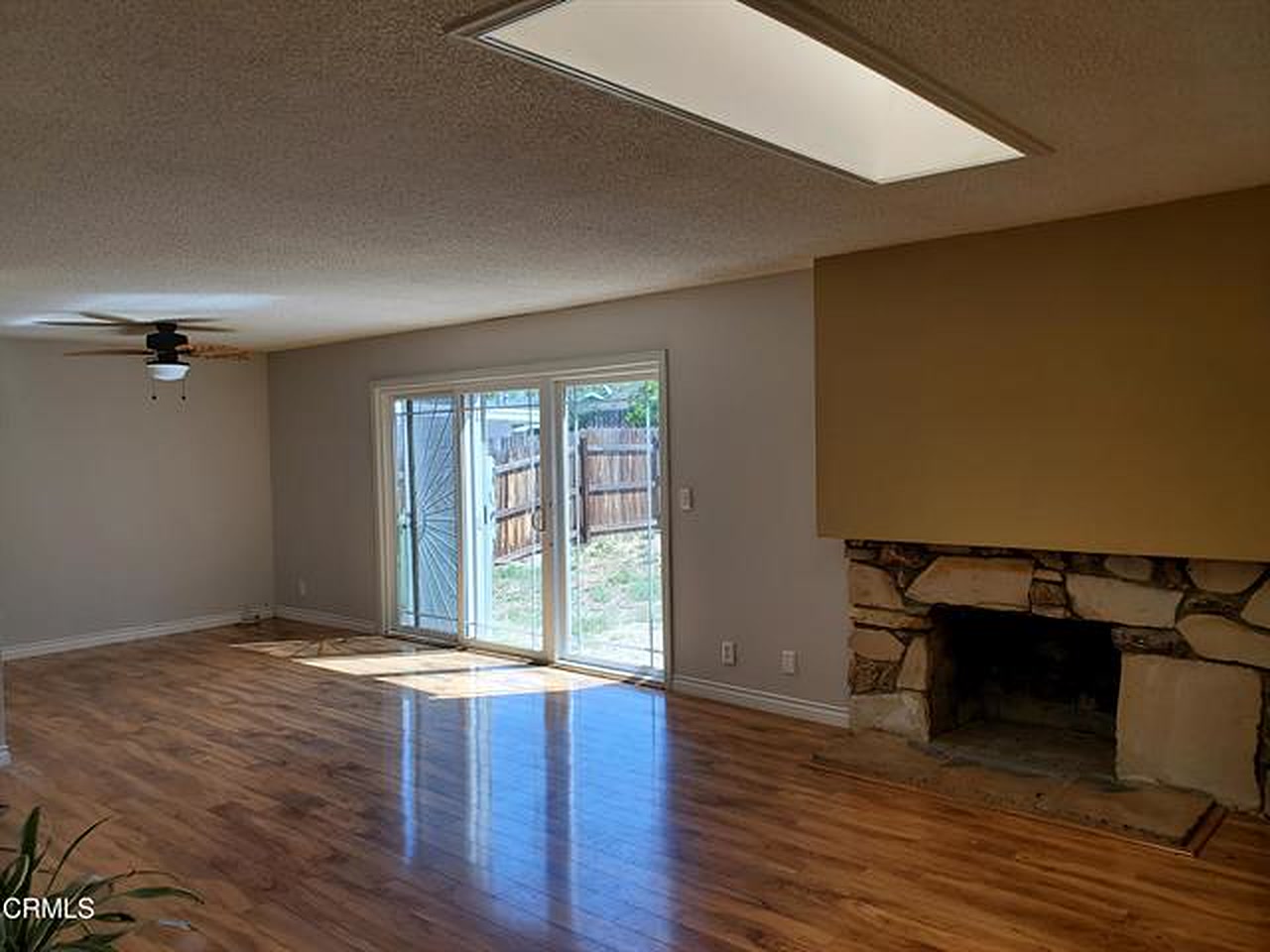 The living room in 2022: the stone fireplace under a painted bump-out, textured ceiling, and a sliding door to the rear yard.