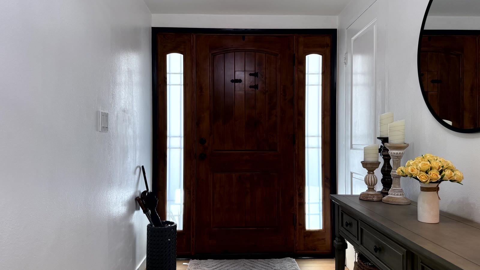 Entry foyer with a stained wood front door flanked by two full-height sidelights, black casing, white walls and wood-look plank flooring.