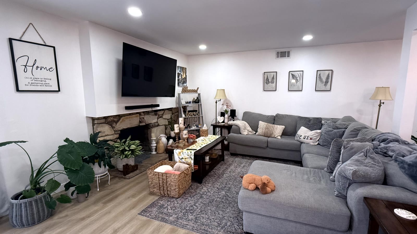 Living room with a floor-to-mantel rough-cut stone fireplace on a raised hearth, plaster chimney breast above, recessed ceiling lights and wood-look plank flooring.